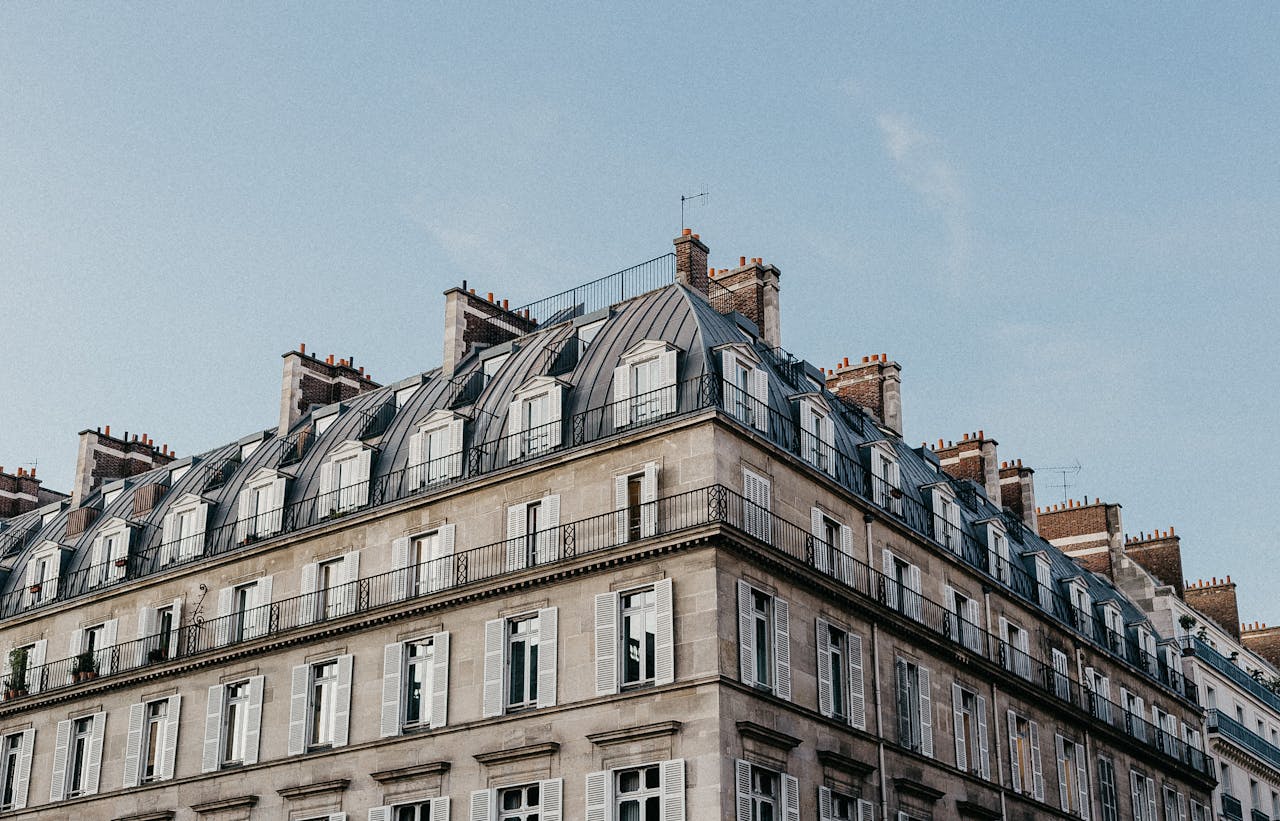 our-journey-03 Elegant Parisian architecture featuring a classic Mansard roof and stone facade under a clear blue sky.