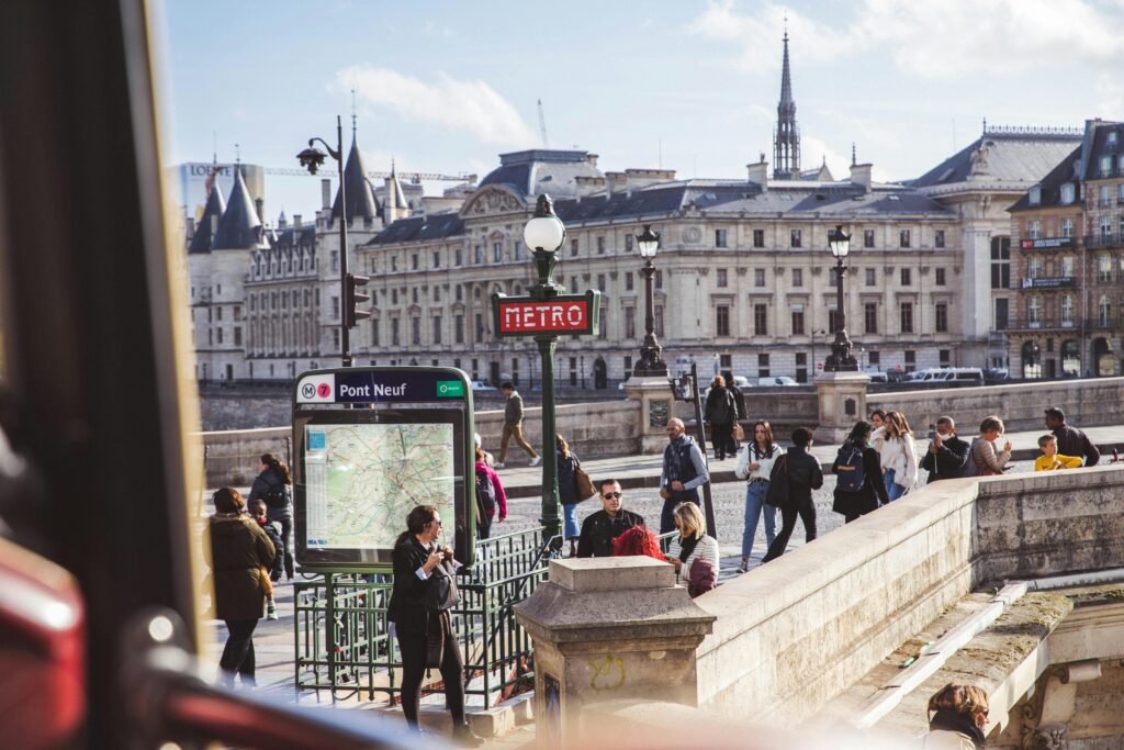 pexels-photo-14433882-14433882 Vibrant scene at Paris Pont Neuf with pedestrians near Metro entrance and historic architecture.