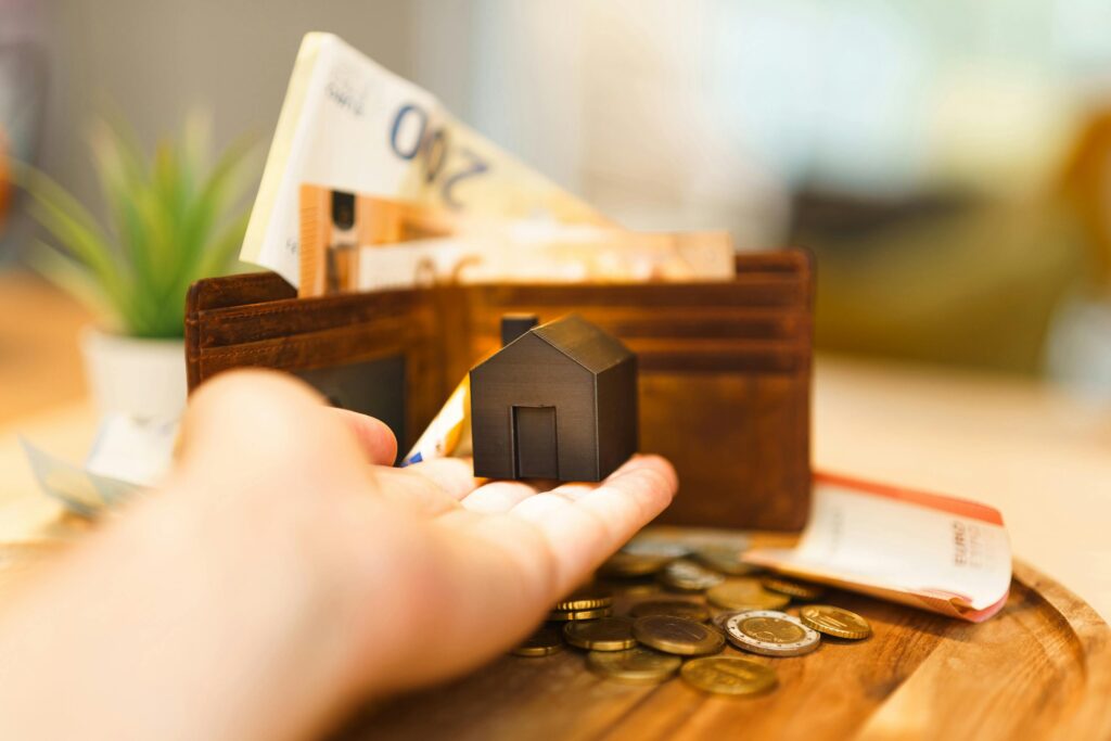 pexels-photo-30139495-30139495 A hand holding a small house model with euro notes and coins nearby, illustrating real estate investment and finance.